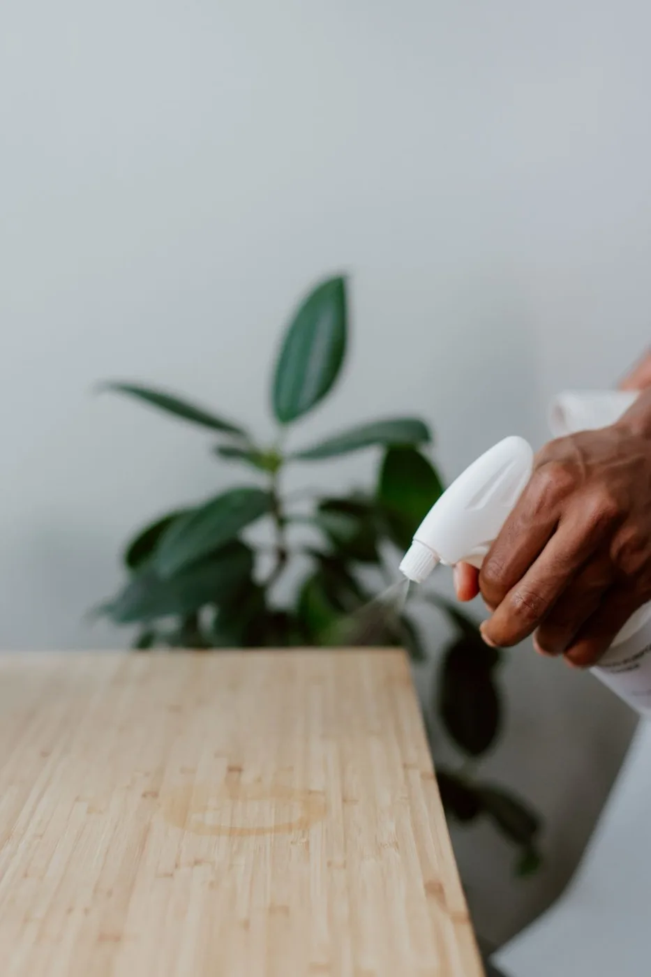 A gloved hand spraying and wiping a wooden table