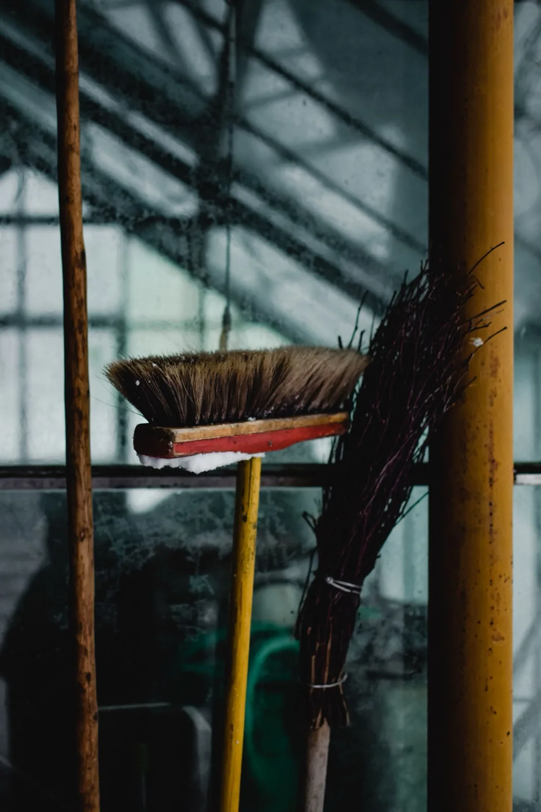 A broom and a hand brush leaning against a window